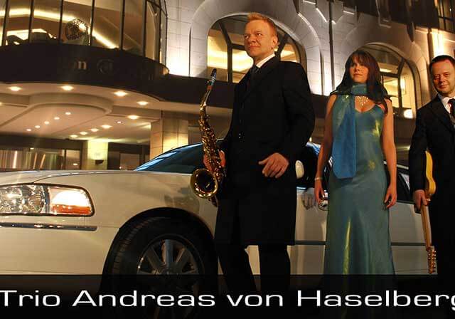 Hochzeitsband als Trio – Saxophonist, Sängerin und Gitarrist – vor einer weißen Stretchlimousine